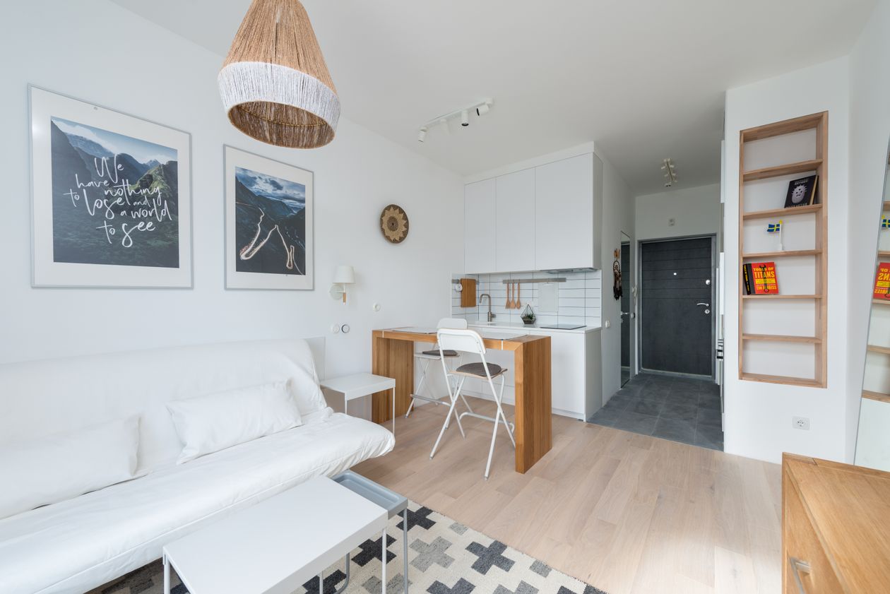 Bright minimalist studio with a white sofa, fold-down table and wall shelves, a space saving storage and organization idea